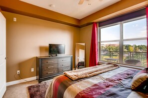 A bedroom with a bed, a dresser, a television, and a window with a view of the outdoors.