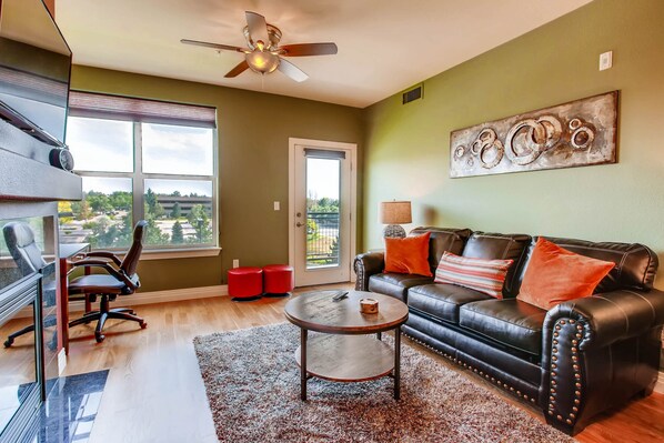 A living room with a leather sofa, a coffee table, a TV, and a view through a large window.