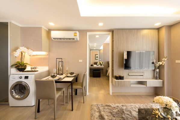 A modern living room with a flat-screen TV, a washing machine, and a dining area with chairs and a table. - Residence 187 (Bangkok)