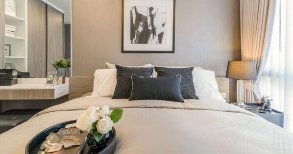 A hotel room with a neatly made bed, a bedside table with a lamp, a framed artwork on the wall, and a window with curtains. - Residence 187 (Bangkok)