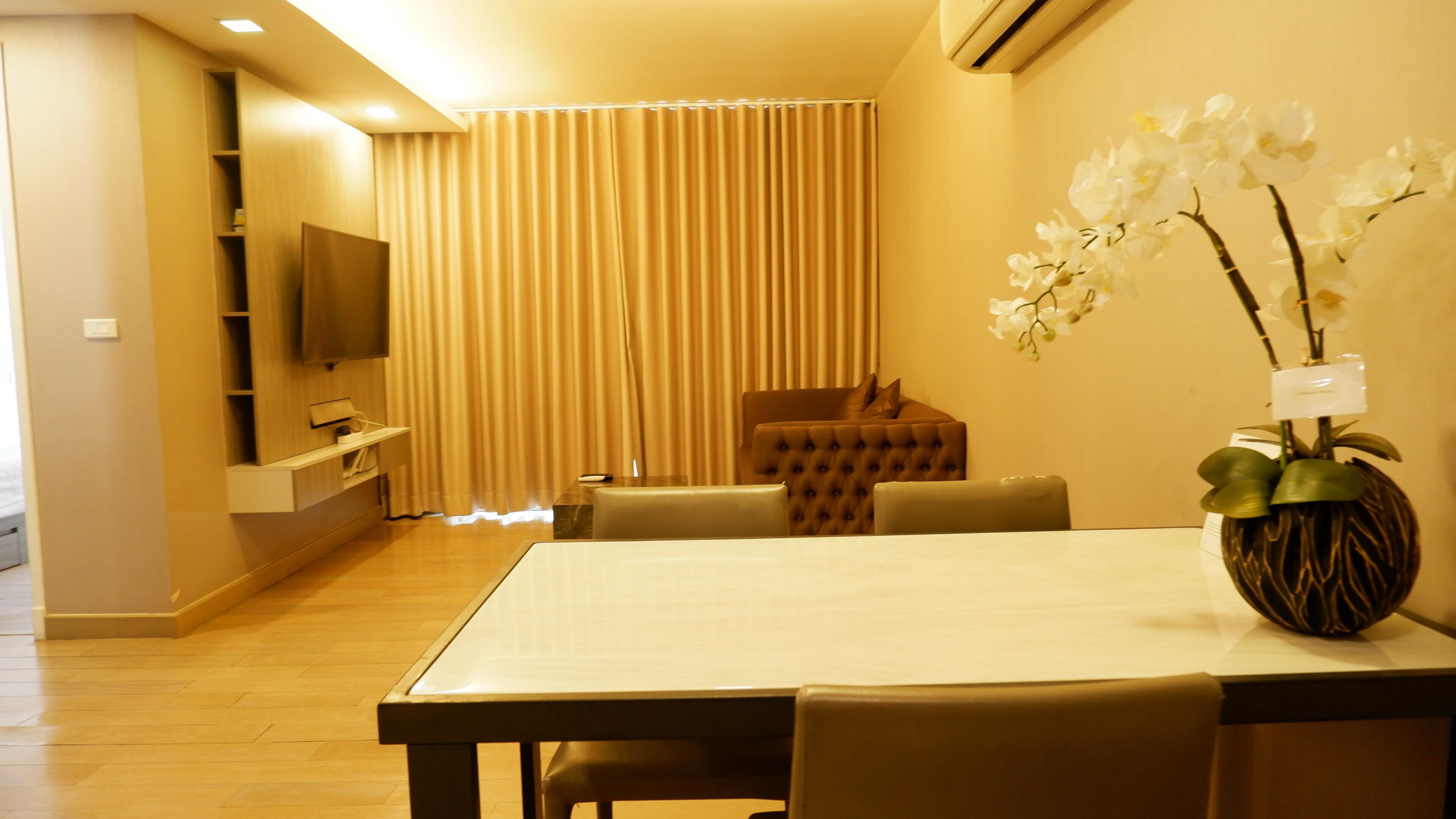 A modern living room with a flat-screen TV, a dining table, and a sofa.