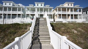 A wooden staircase leading to a beachfront property with multiple balconies and a white fence.