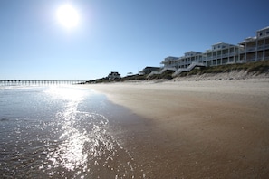 A beach with a pier extending into the water, beachfront properties, and a clear sky. - Oceanfront Home,Early Check-In, Pool, Elevator, 50 Steps to the Beach (Surf City)