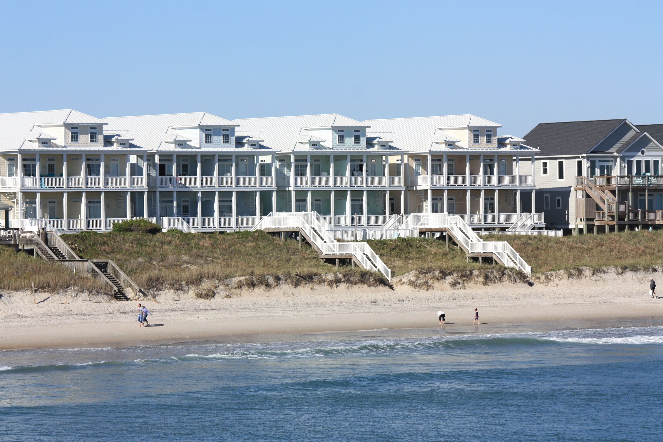 Un hôtel situé en bord de mer, doté de nombreux balcons, d’une plage de sable et offrant une vue sur un ciel dégagé.