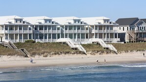 A beachfront hotel with multiple balconies, a sandy beach, and a clear sky.