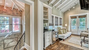 A spacious living area with a kitchen, a dining area, and a staircase leading to an upper level. - Modern Luxury Oasis: Outdoor Fire Pit Overlooking Camp WaterColor Pool and Park. (Santa Rosa Beach)