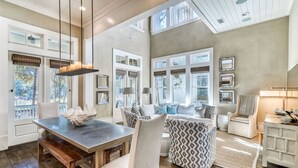 A spacious living room with a dining area, large windows, and a high ceiling. - Modern Luxury Oasis: Outdoor Fire Pit Overlooking Camp WaterColor Pool and Park. (Santa Rosa Beach)