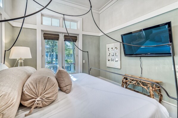 A bedroom with a bed, a TV mounted on the wall, and a window with blinds.