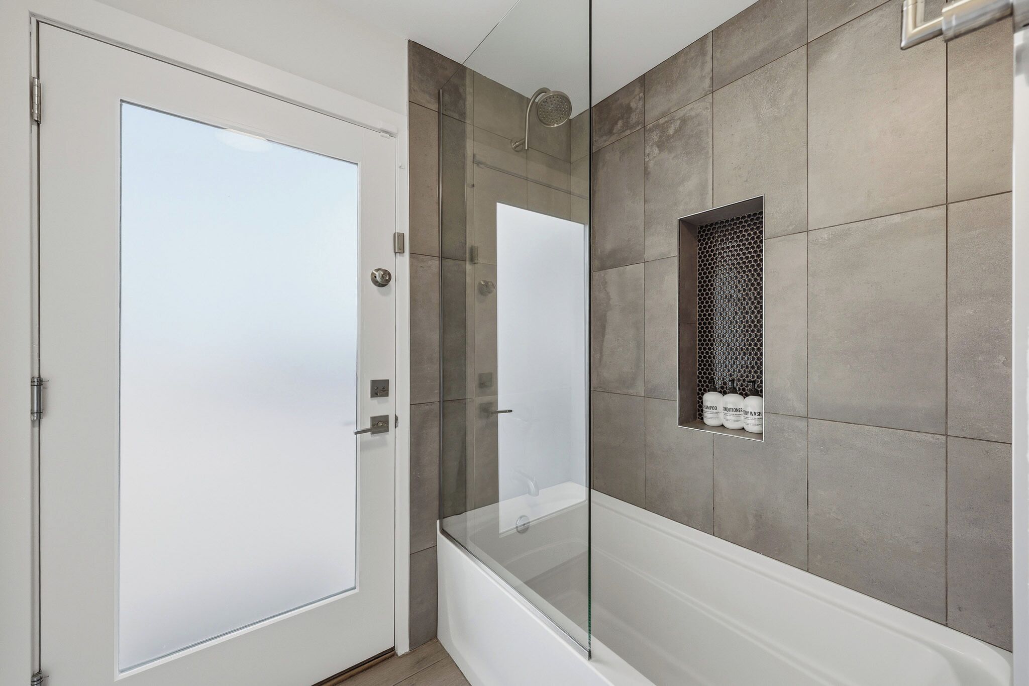 A modern bathroom with a glass-enclosed shower, a white door, and a shelf with toiletries.
