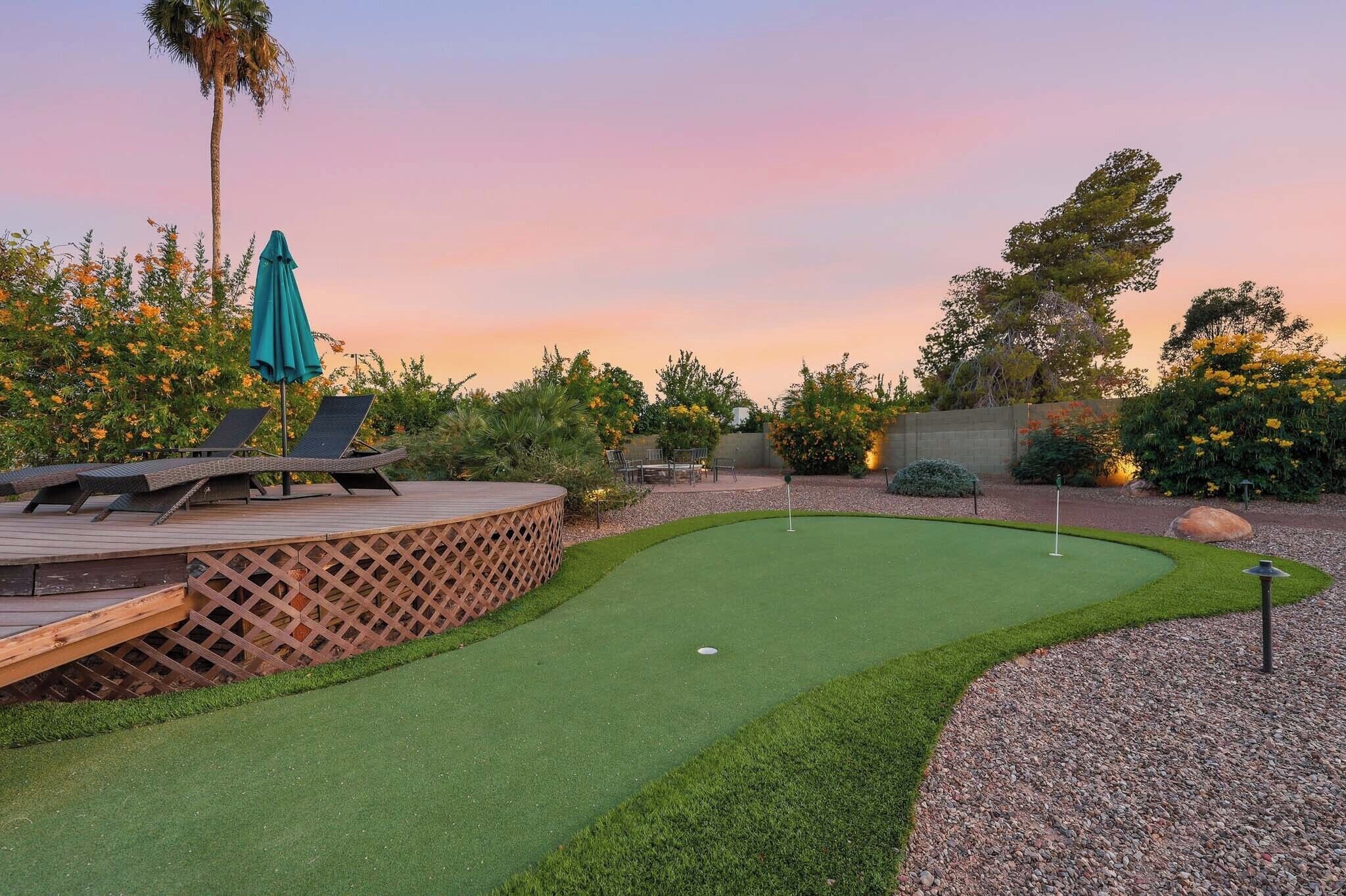 A backyard with a putting green, lounge chairs, and a wooden deck.