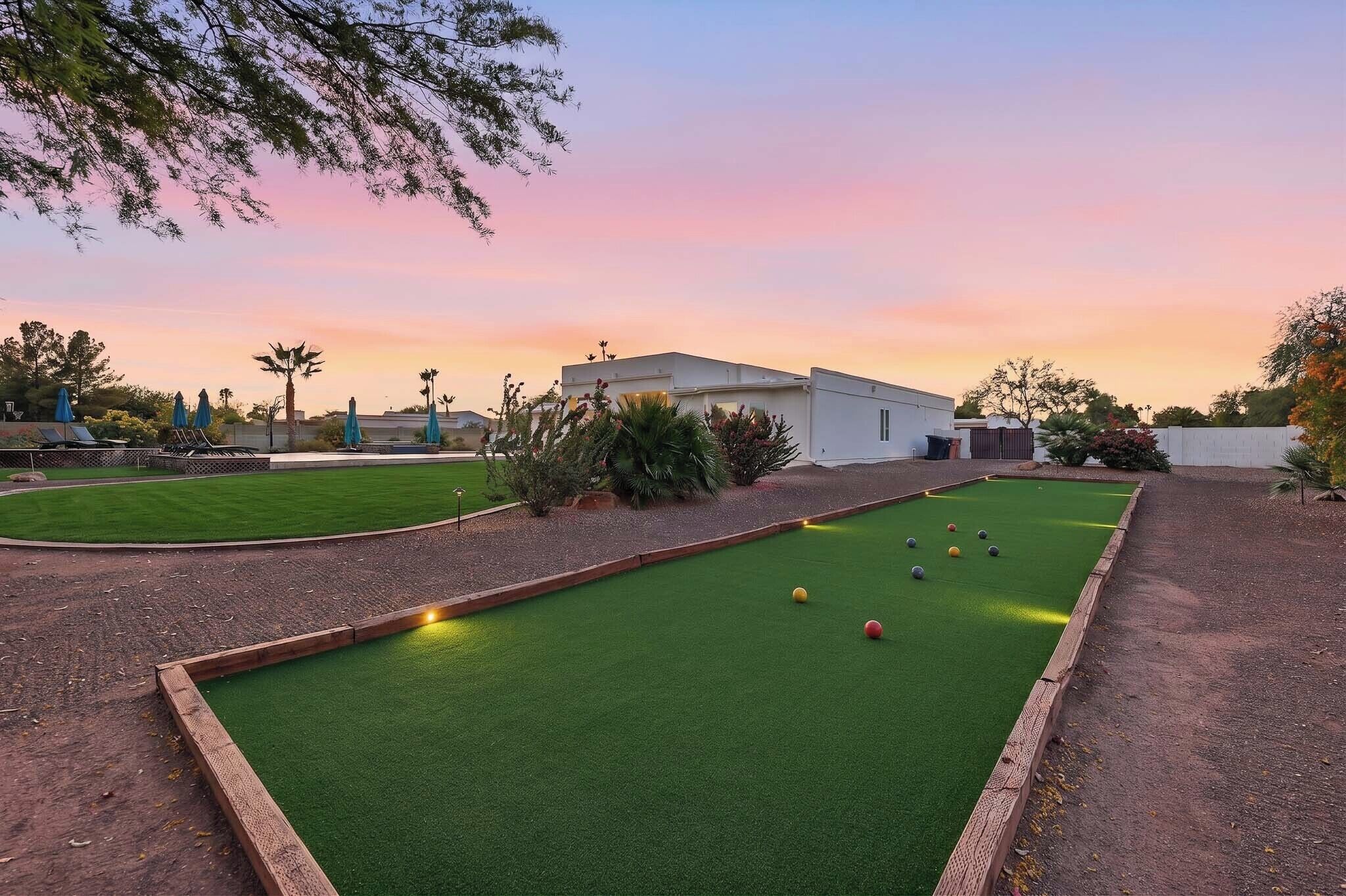 A pool table with balls, surrounded by a green lawn and a building in the background.