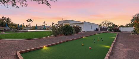 A pool table with balls, surrounded by a green lawn and a building in the background.