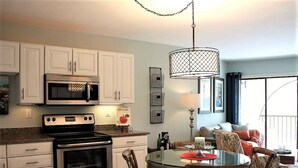 A modern kitchen with stainless steel appliances, a dining area with a glass table, and a balcony with a view. - PARADISE-Anglers Cove Waterfront Designer Condo (Marco Island)