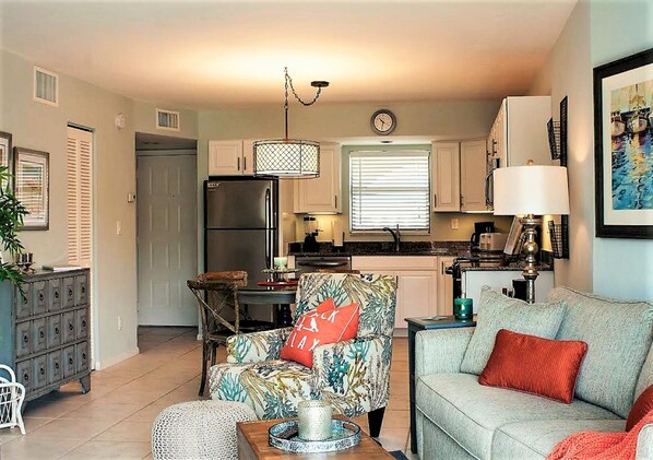 A modern kitchen with white cabinets, a stainless steel refrigerator, and a dining area with a table and chairs.