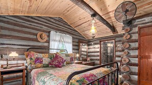 Un dormitorio de cabaña de madera con cama, mesita de noche, lámpara, ventilador y espejo.