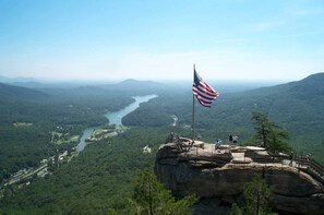 Un mirador panorámico con una bandera sobre un afloramiento rocoso, con vista a un río y un valle boscoso.