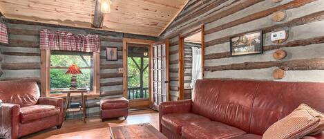 A log cabin interior with a leather sofa, a wooden coffee table, and a plaid-patterned rug.