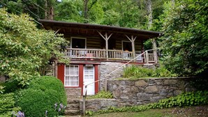 Una cabaña rústica con cimientos de piedra, una terraza de madera y una puerta roja.