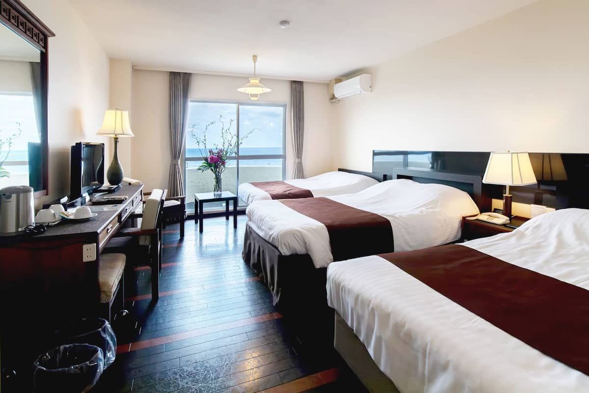 Ein Hotelzimmer mit zwei Betten, einem Schreibtisch mit Computer, einer Kaffeemaschine und Meerblick.