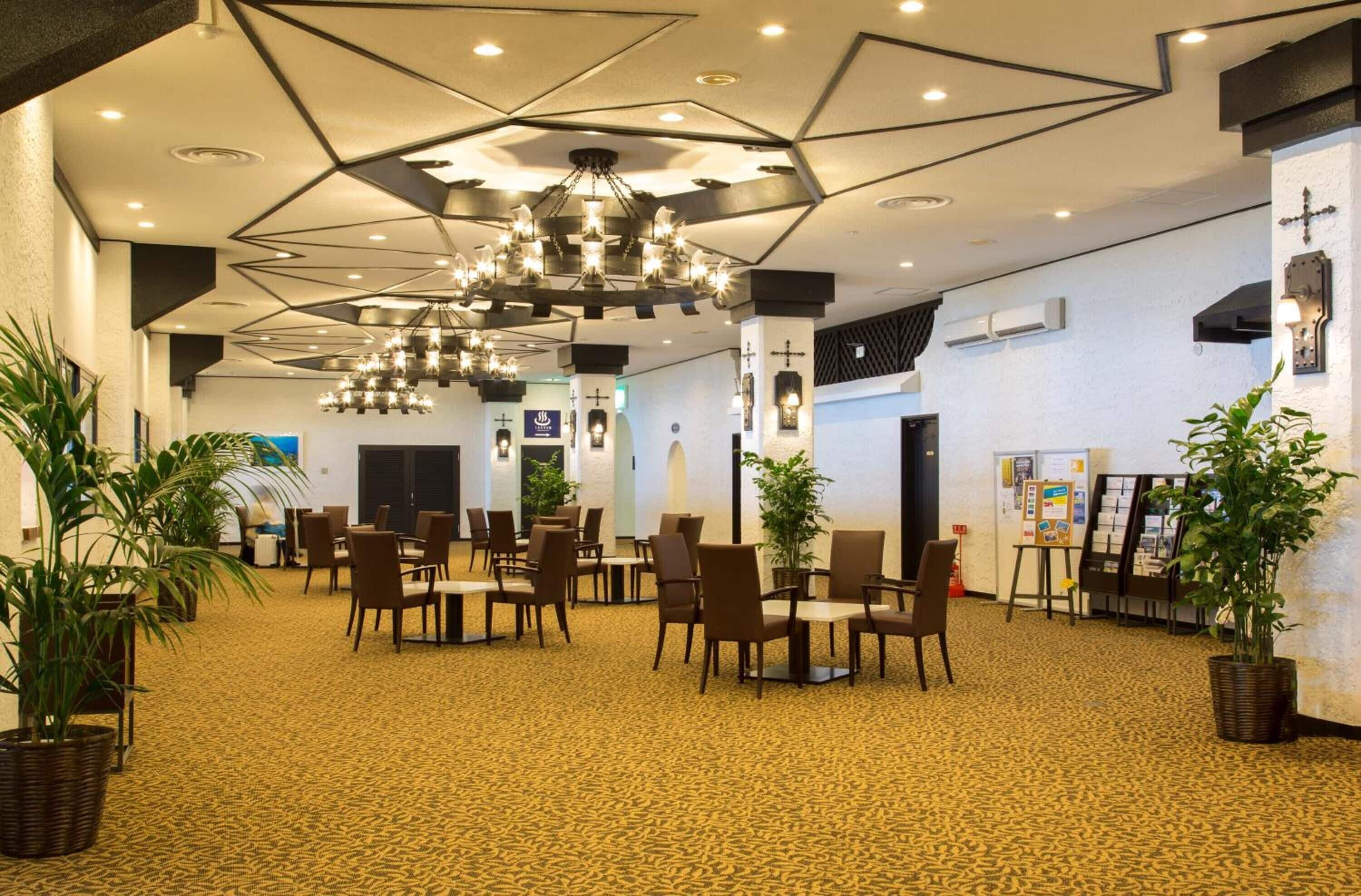Un hall d’entrée spacieux, doté d’un plafond au design géométrique, de plusieurs espaces aménagés pour s’asseoir et de nombreuses plantes en pot.
