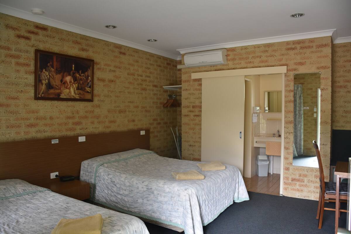 A hotel room with two beds, a painting on the wall, a bathroom with a mirror, and a desk with a chair.
