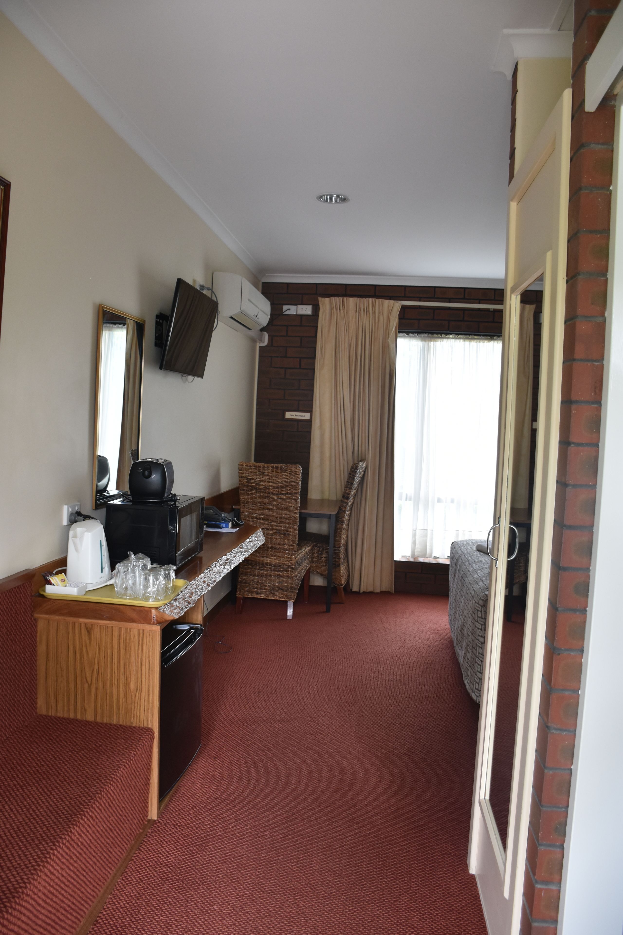 Habitación de hotel con kitchenette, una cama, una silla, una mesita y una ventana con cortinas.
