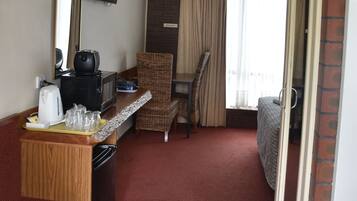 Habitación de hotel con kitchenette, una cama, una silla, una mesita y una ventana con cortinas.