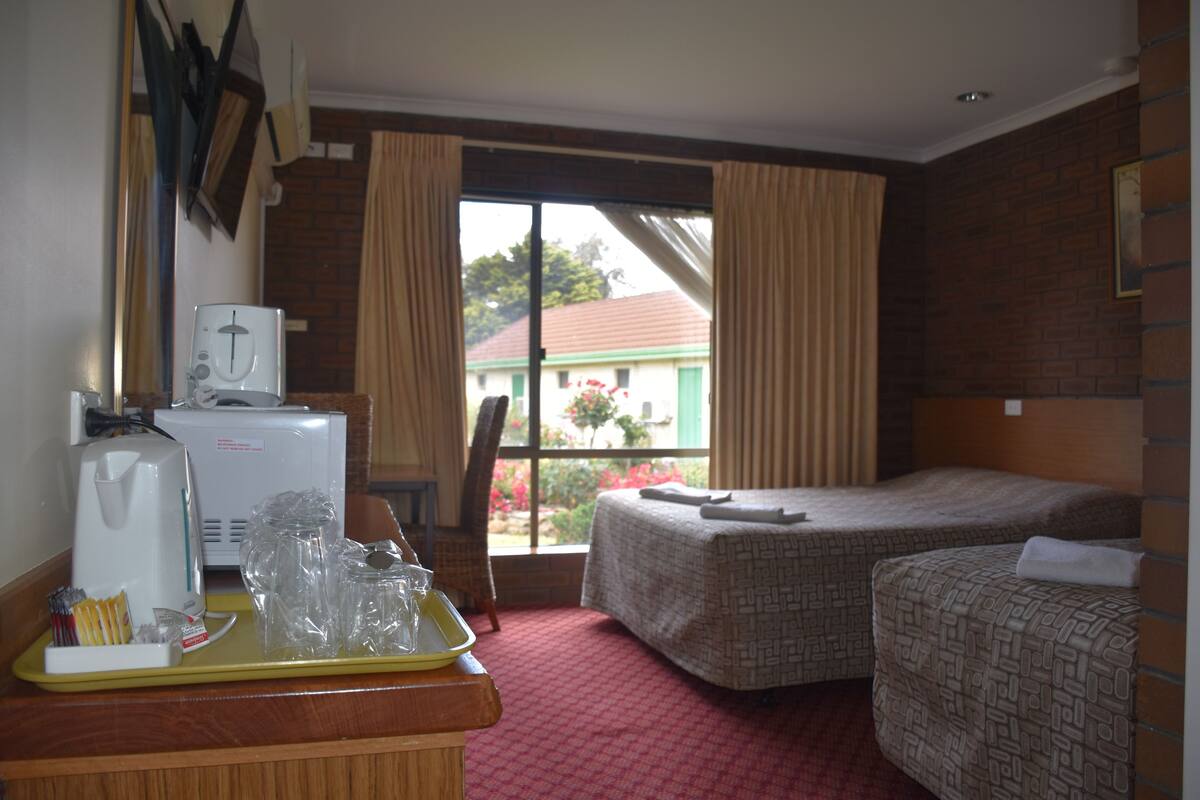 A hotel room with a bed, a desk with a coffee maker, and a window with curtains.