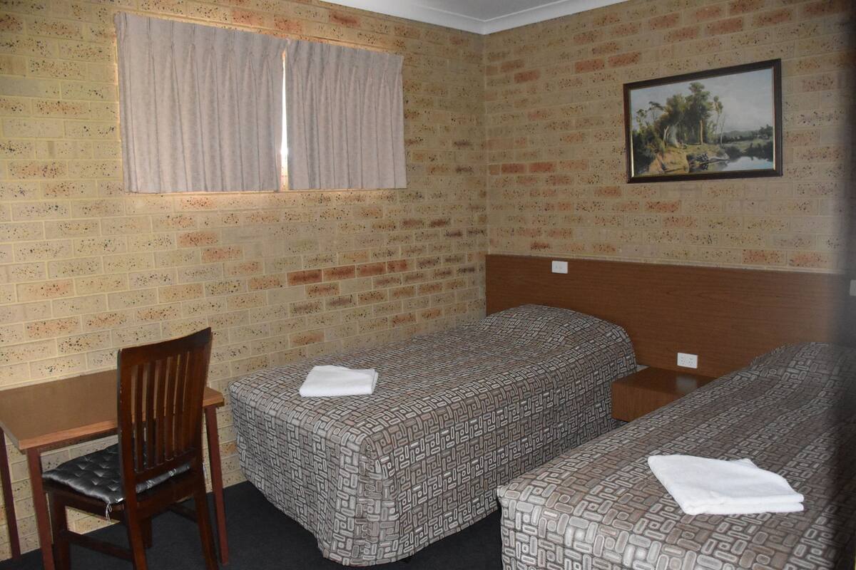 A room with two beds, a desk, a chair, and a window with curtains.