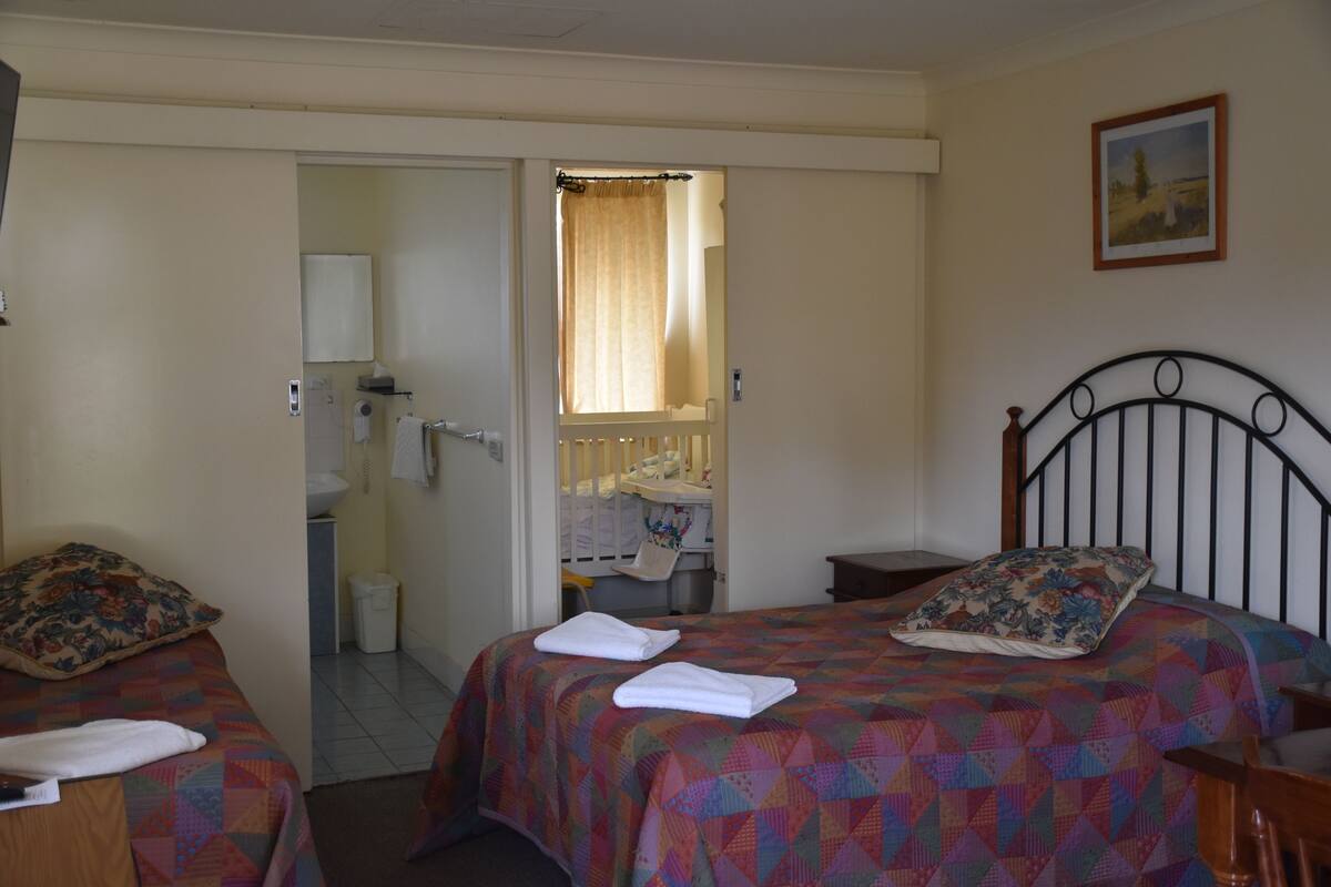 A bedroom with two beds, a bathroom visible through an open door, and a painting on the wall.