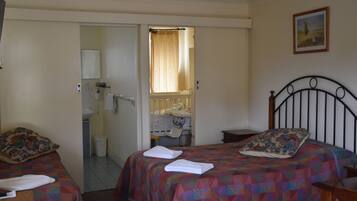 A bedroom with two beds, a bathroom visible through an open door, and a painting on the wall.