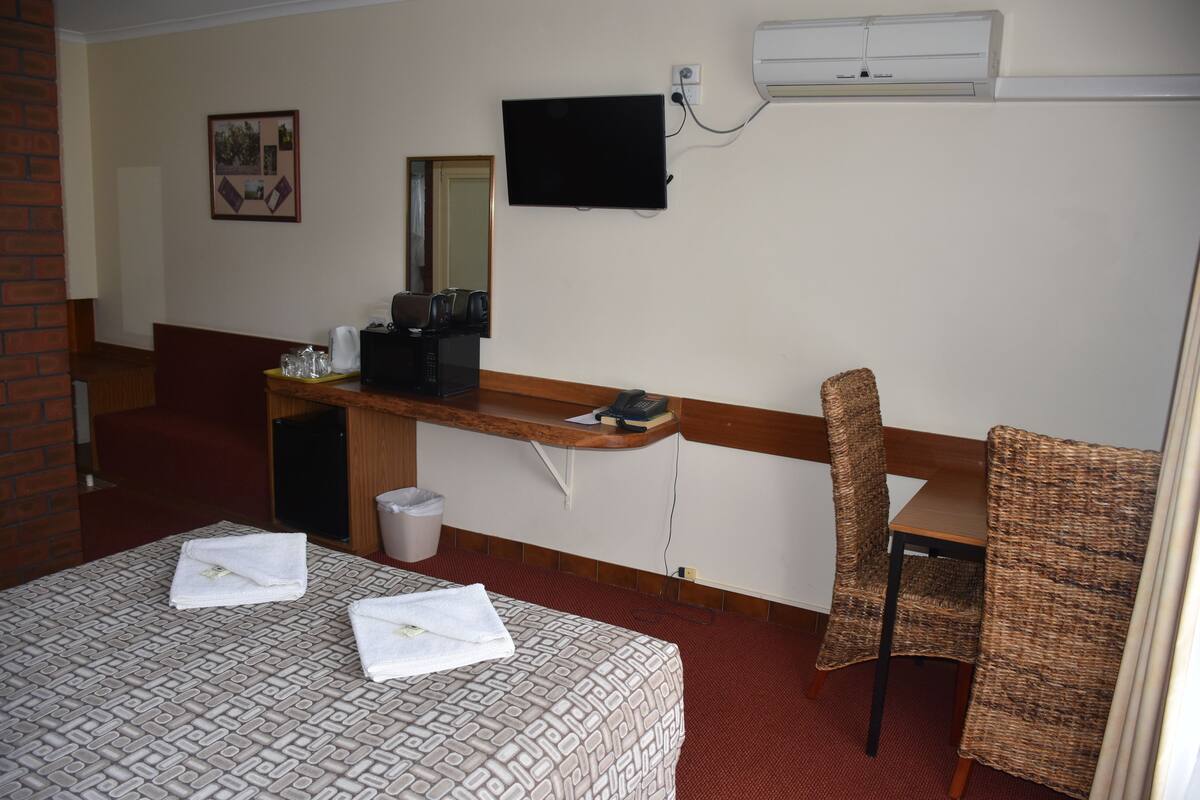 A hotel room with a bed, a desk, a chair, a television, and a trash can.