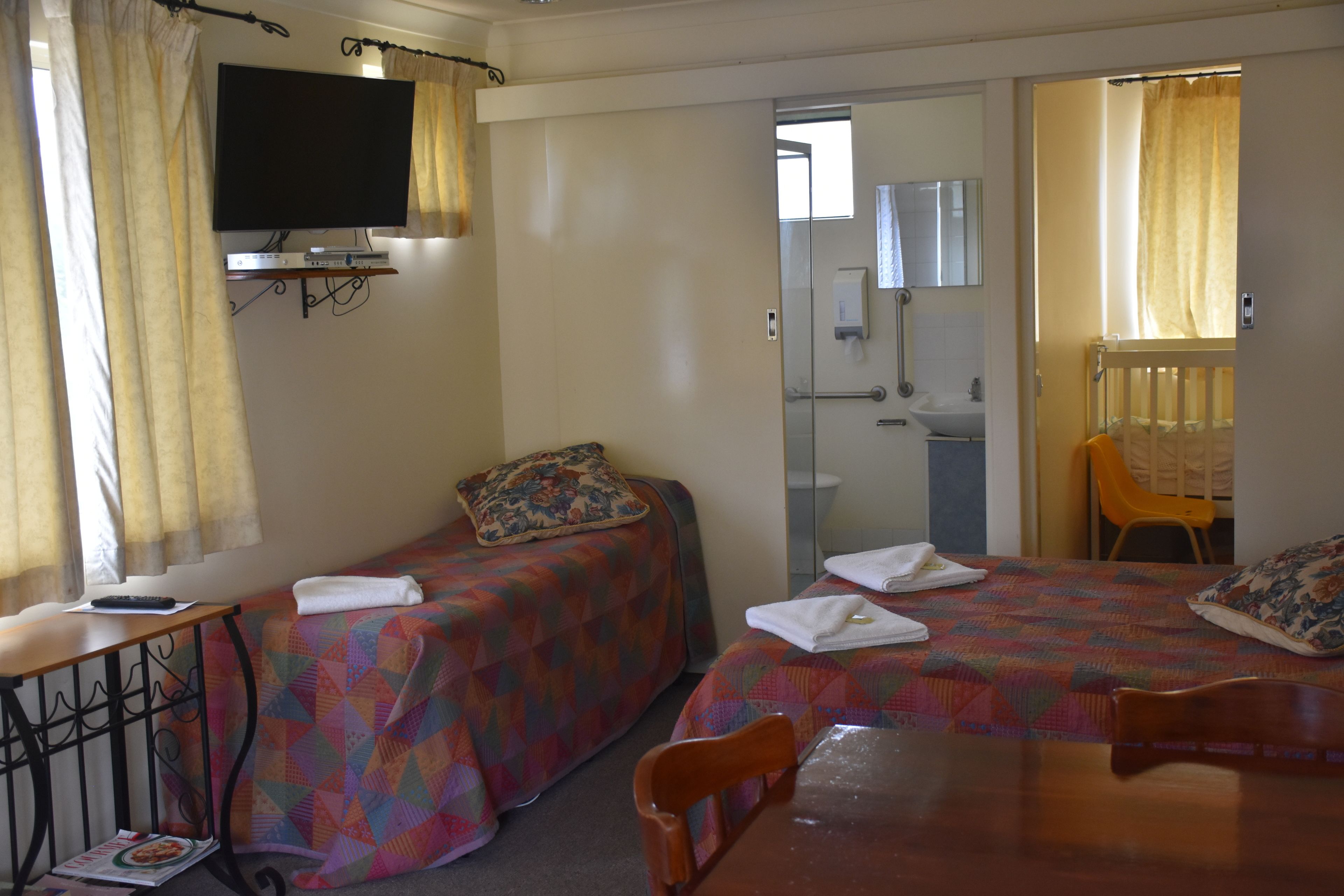 A hotel room with two beds, a TV, a small table, and a bathroom visible through an open door.