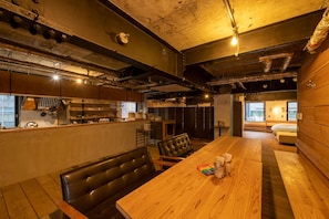 A cozy restaurant with a wooden dining table, black leather booth seating, and a kitchen area visible through the open counter. - Kagoshima Guest House M104 - Hostel (Kagoshima)