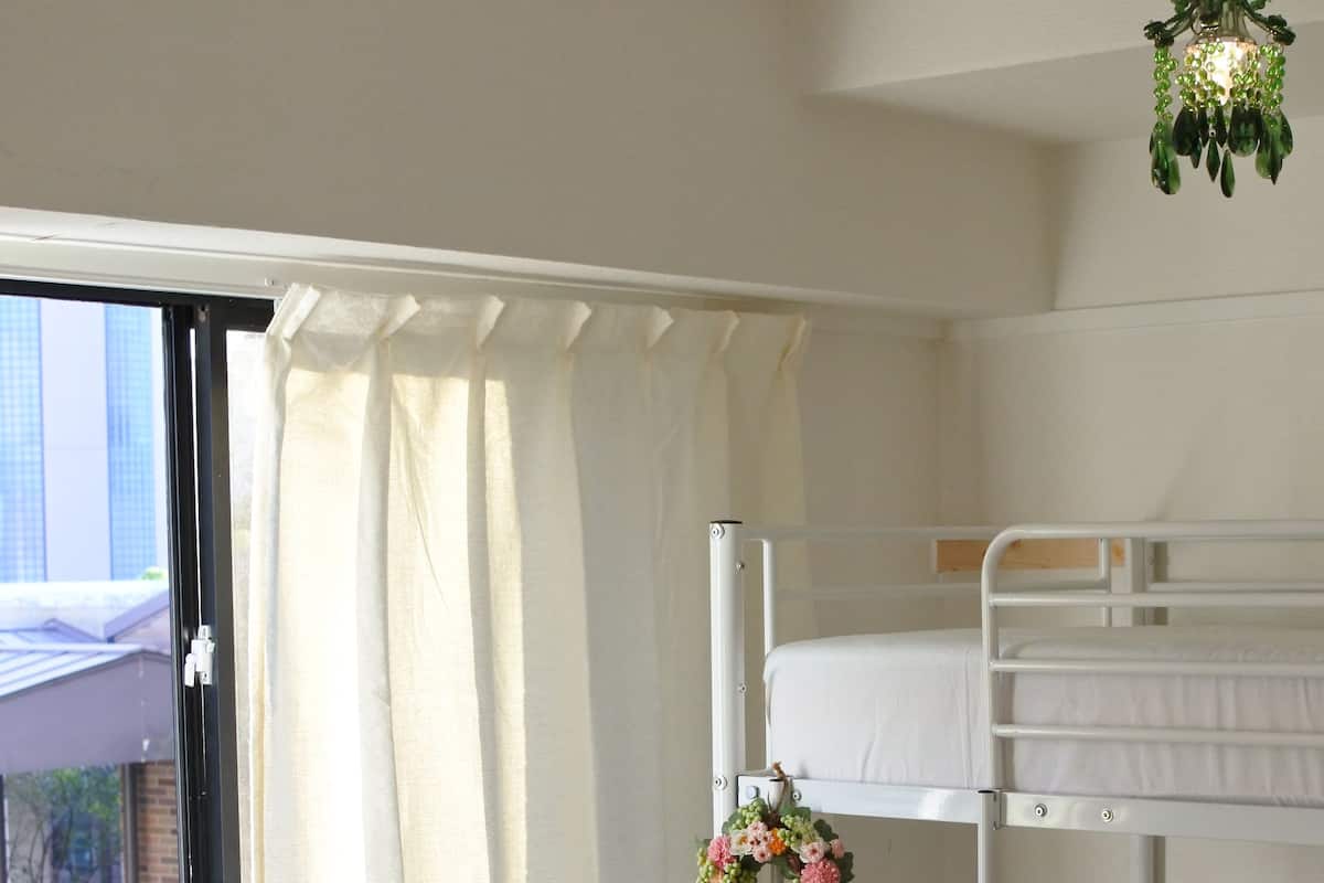 A bunk bed room with a window, curtains, and a hanging plant.