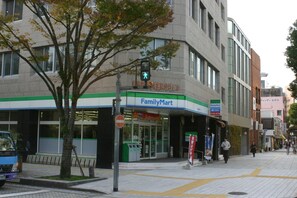 A FamilyMart store with a green and white sign, located on a city street with a pedestrian crossing and a traffic light. - Kagoshima Guest House M104 - Hostel (Kagoshima)