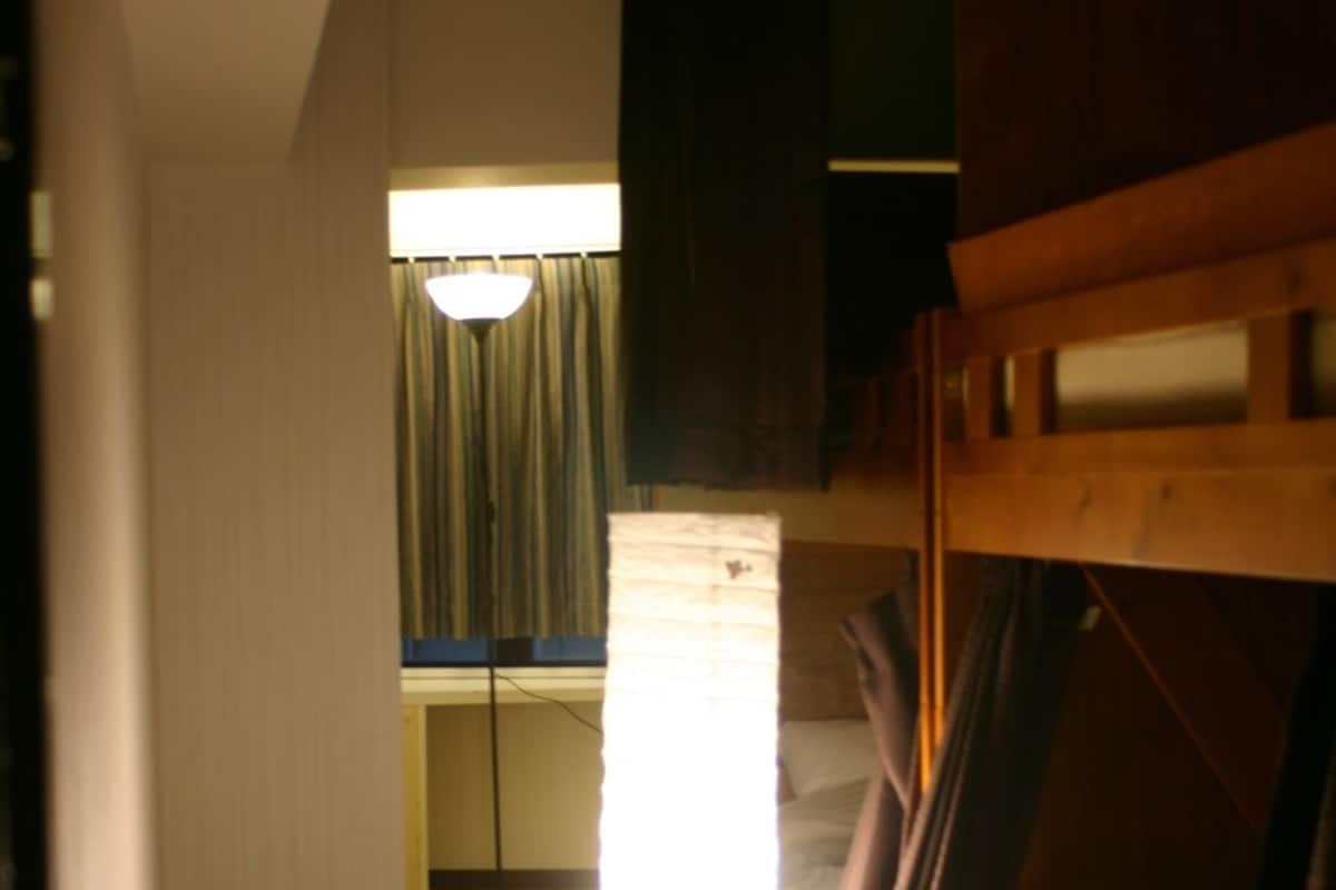 A hotel room with a bunk bed, a standing lamp, and a window with curtains.
