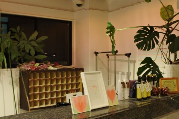 A hotel reception area with a plant display, framed artwork, and various bottles on the counter. - Kagoshima Guest House M104 - Hostel (Kagoshima)