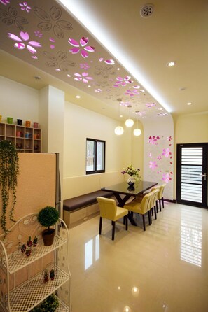 A modern dining area with a long table, chairs, pendant lights, and a decorative ceiling.