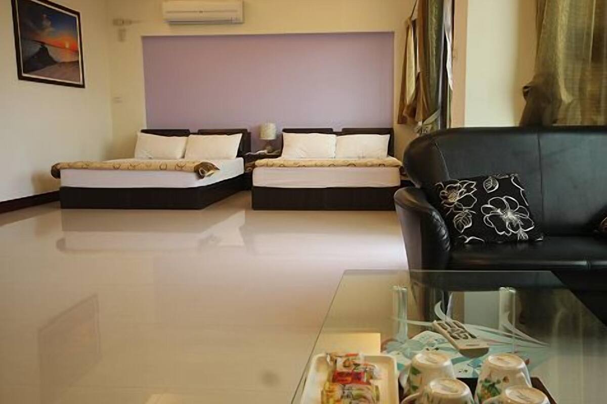 A hotel room with two beds, a black leather sofa, a glass coffee table, and a painting on the wall.
