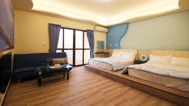 A modern hotel room with a sofa, two beds, a coffee table, and a large window. - Sweet Dream Homestay (Magong)