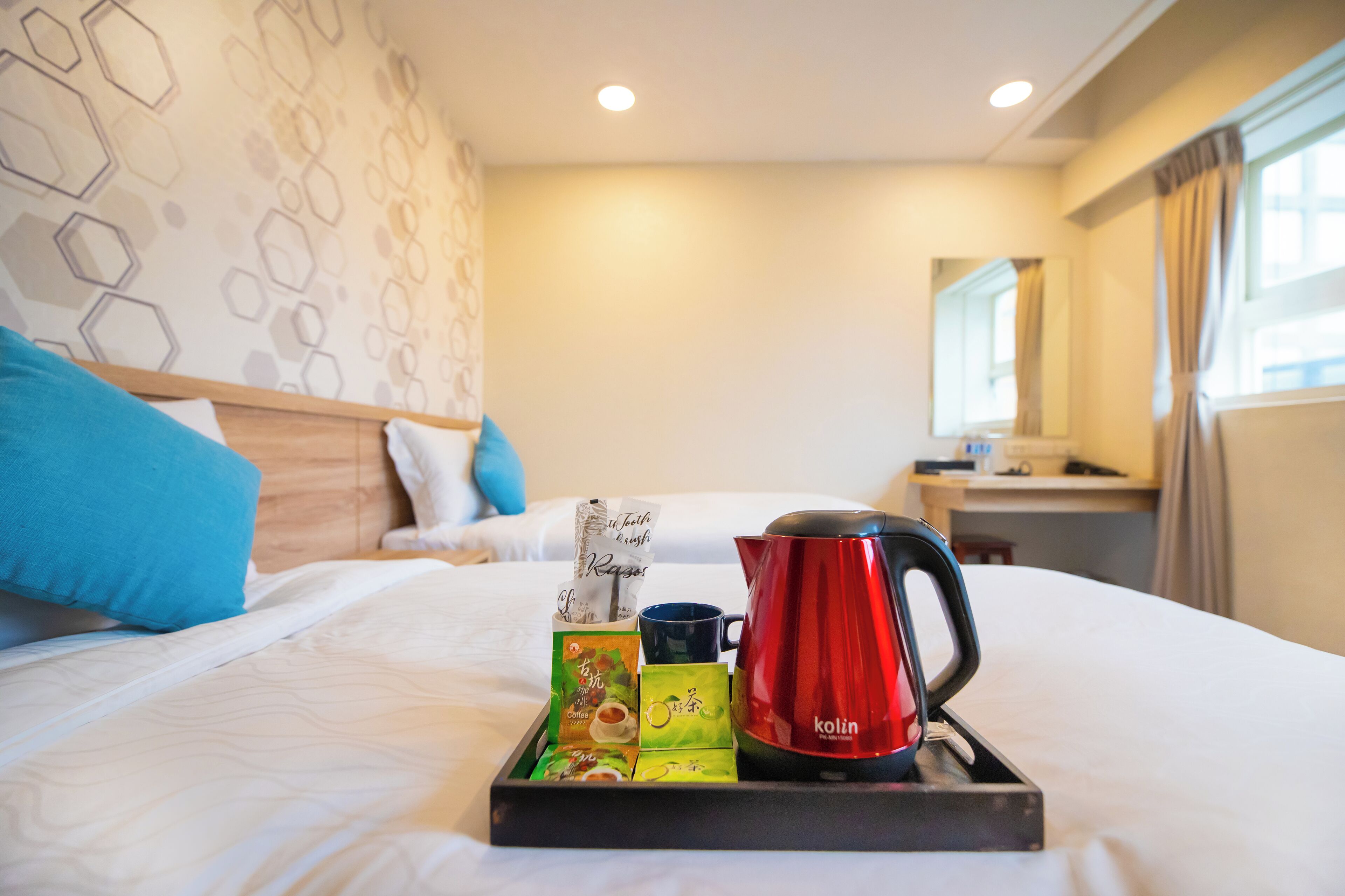 A hotel room with a bed, a tray with tea and snacks, and a red kettle.