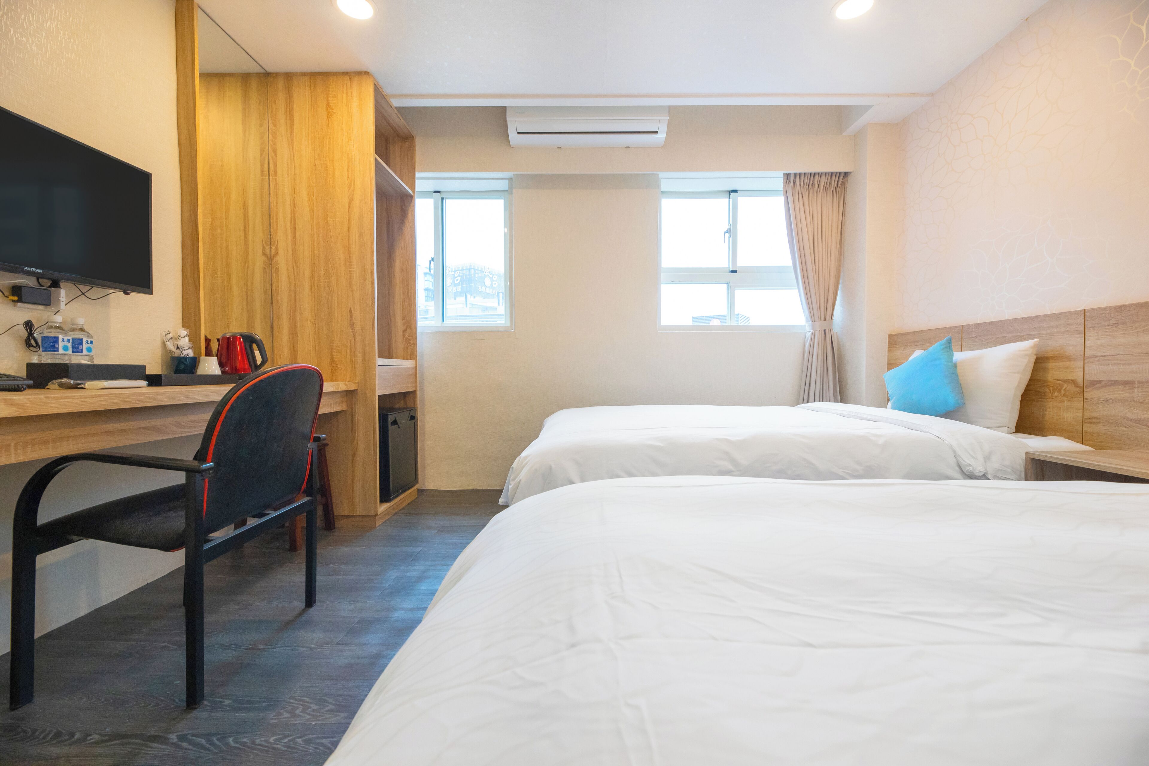 Habitación de hotel con dos camas, un escritorio con silla, televisor y ventana con cortinas.