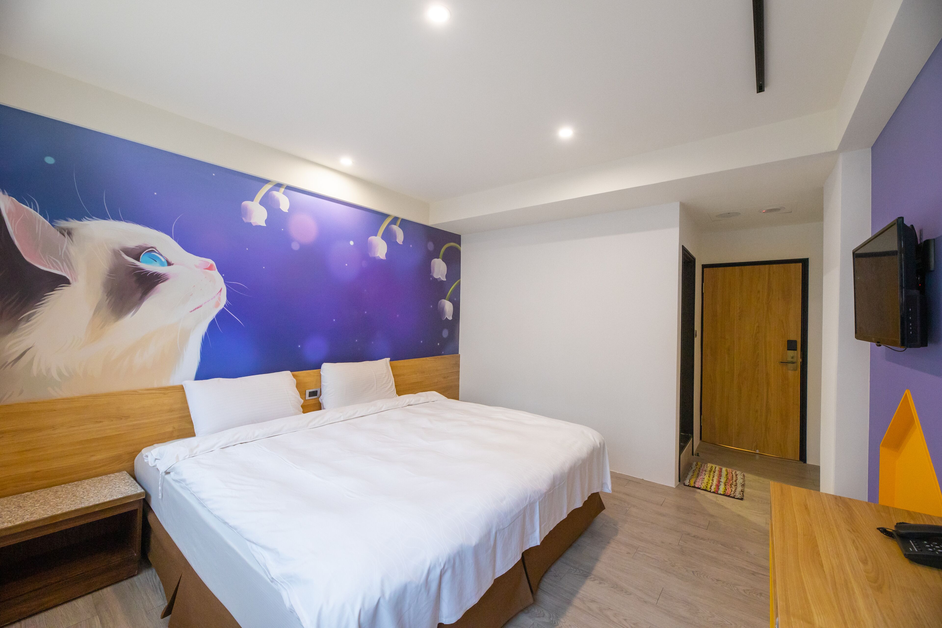 Une chambre d’hôtel avec un grand lit, une tête de lit en bois, une fresque murale, un téléviseur et une porte en bois.