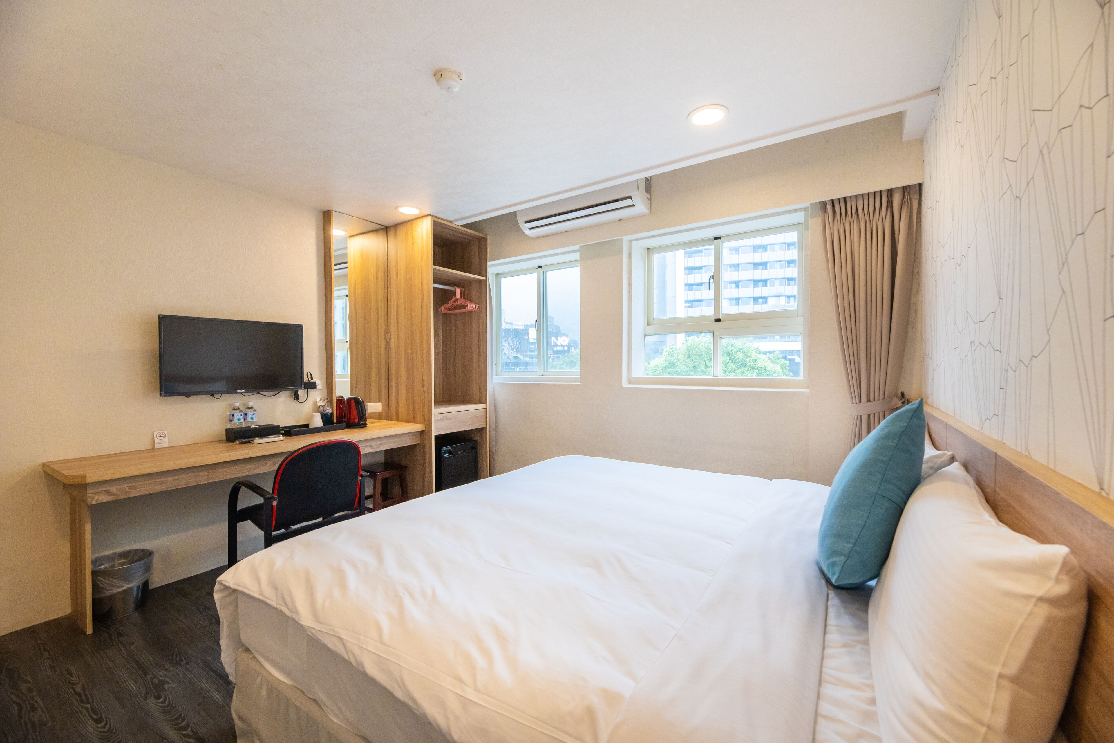 A hotel room with a bed, a desk with a chair, a TV, and a window with curtains.