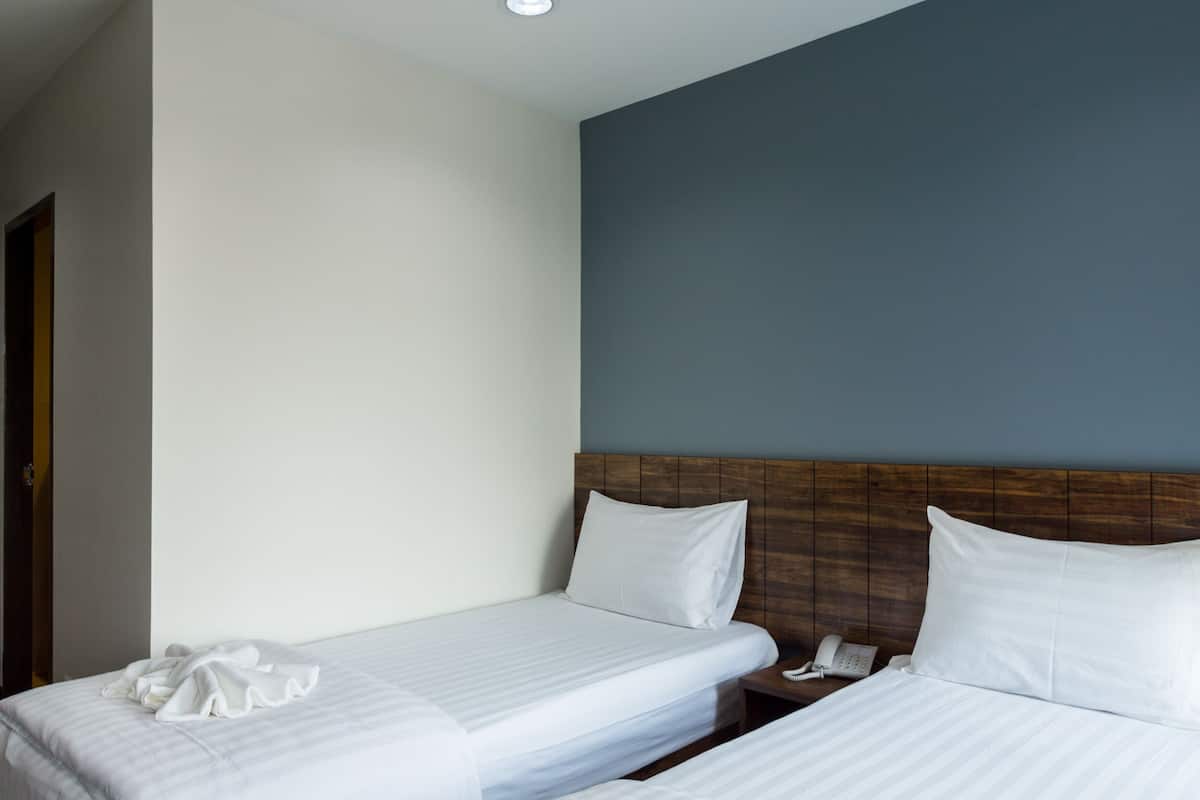 Habitación de hotel con dos camas individuales, un cabecero de madera, una mesita de noche con teléfono y una puerta a la izquierda.