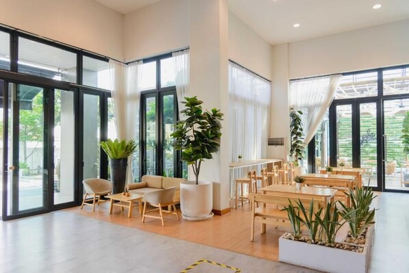 A spacious indoor area with large windows, a seating area with tables and chairs, and potted plants. - Glai Gan Place Hotel (Saraburi)