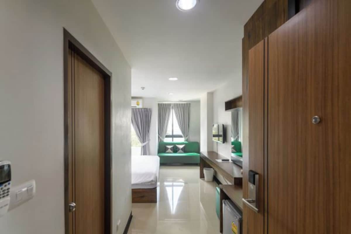 A hotel room with a bed, a green sofa, a desk with a computer, and a TV.