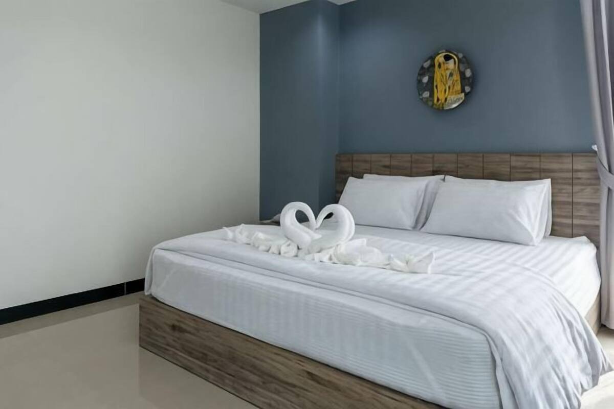 Una cama bien hecha con sábanas blancas y un diseño decorativo de cisne, un cabecero de madera y un reloj de pared.