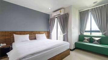 Une chambre d’hôtel avec un lit, un canapé vert, une table de chevet et un appareil de climatisation.